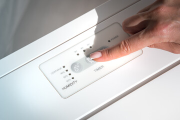 Woman turning on air dryer, purifier, dehumidifier, humidity indicator, air ionizer or water...