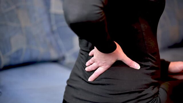 The woman rubs her back. A woman is sitting on the couch with back pain.