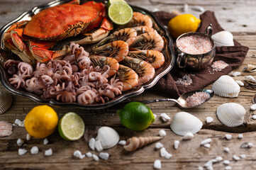 Appetizing view of plate with tasty assorted seafood served with lime, lemon, sea salt and seashells on rustic wooden background. Seafood concept. Delicious meal. Flat lay. Space for text.