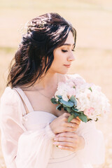 Portrait of the bride in a powdery dress with a wedding bouquet in her hands on the background of nature