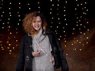 A beautiful curly-haired girl stands on a black background in the New Year's lights