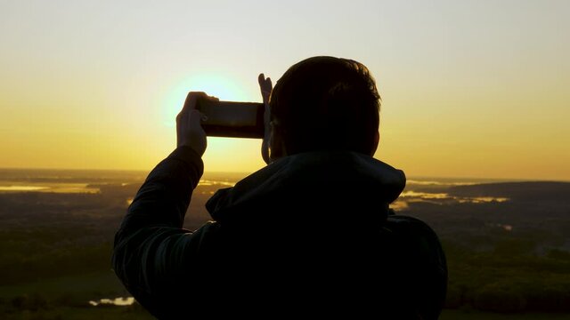 traveler takes photos and videos on his smartphone at dawn, from the mountain in rays of the beautiful sun. A free peasant tourist enjoys a beautiful view of nature from a high hill. travel concept