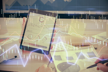 Double exposure of man's hands holding and using a digital device and forex graph drawing....