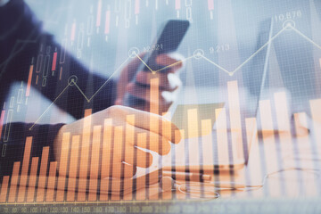 Double exposure of man's hands holding and using a phone and financial graph drawing. Analysis...
