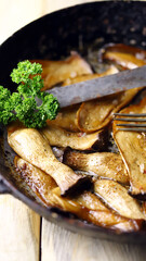 Fried eringi mushrooms in a frying pan on a wooden surface.