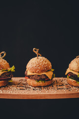 One burger on a wooden stand. Black background.