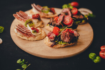 Bruschetta on a round wooden board, black background.