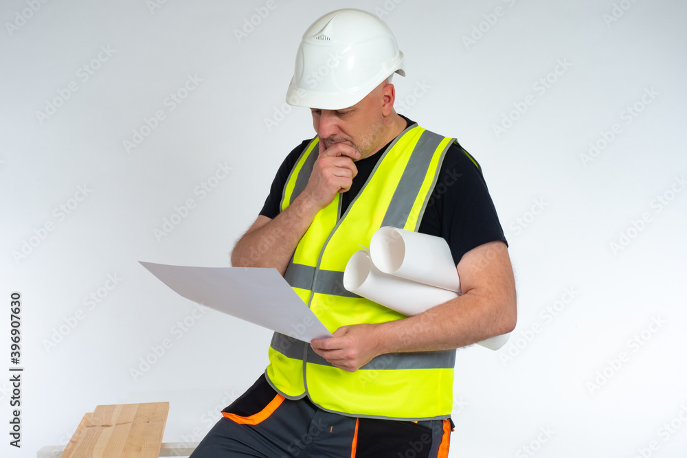 Poster the builder examines the drawings. a man in a work uniform and hard hat with papers in his hands. a 