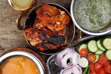 Spicy red Chicken grilled tikka tandoori nan bread green spinach curry yogurt sauce dal tomato cucumber onion salad set in metal stainless steel brass copper pot on rustic vintage wood background