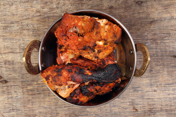 Spicy red Chicken grilled tikka tandoori in metal brass copper pot on rustic vintage wood background