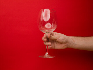 Hand holding an empty wine glass on red background. Side view with space for copying. Concept of holiday backgrounds.