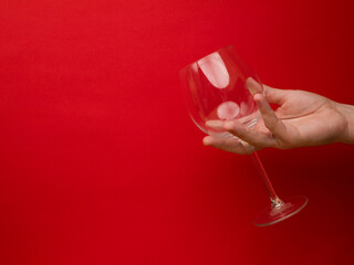 Hand holding an empty wine glass on red background. Side view with space for copying. Concept of holiday backgrounds.