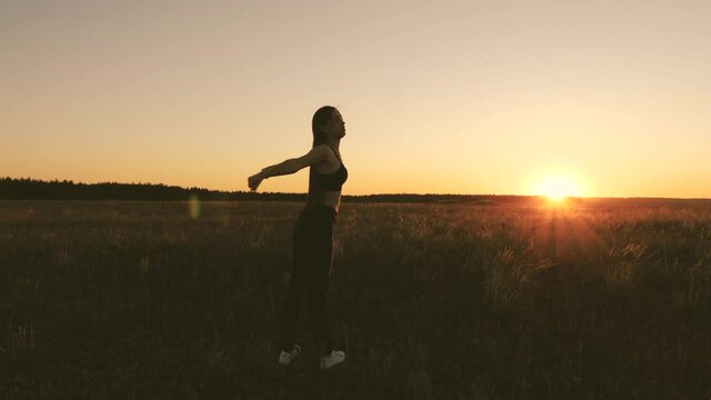 Free young woman goes in for sports in summer park at sunset. healthy beautiful girl is engaged in fitness, outside city in sun. workout and warm-up fresh air. girl breathes fresh air on field.