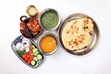 Spicy red Chicken grilled tikka tandoori nan bread green spinach curry yogurt sauce dal tomato cucumber onion salad set in metal stainless steel brass copper pot on white background