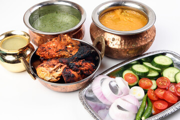 Spicy red Chicken grilled tikka tandoori nan bread green spinach curry yogurt sauce dal tomato cucumber onion salad set in metal stainless steel brass copper pot on white background