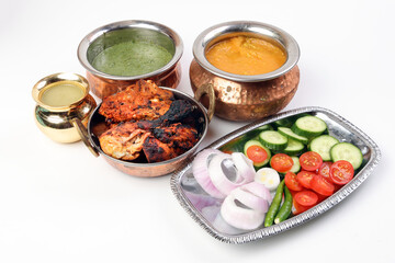 Spicy red Chicken grilled tikka tandoori nan bread green spinach curry yogurt sauce dal tomato cucumber onion salad set in metal stainless steel brass copper pot on white background