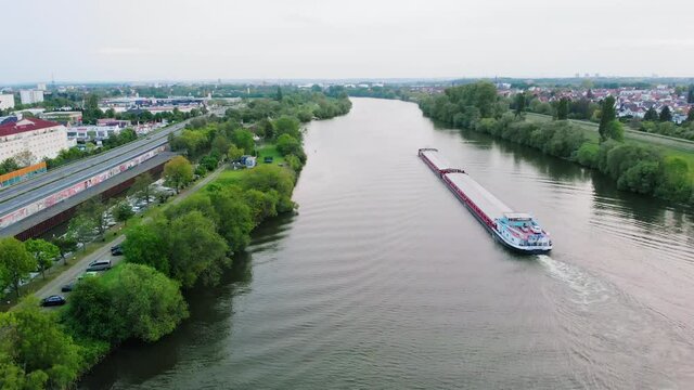 Aerial view of a transport ship on the Main river, cloudy day, in Raunheim town, Germany - pull back, drone shot