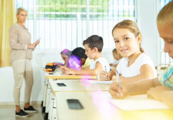 Portrait of diligent schoolgirl sitting in class working with classmates, writing exercise