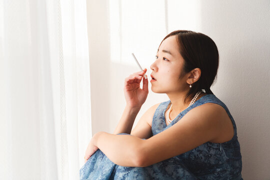 部屋の窓際でタバコを持つ青いドレスを着た若い女性