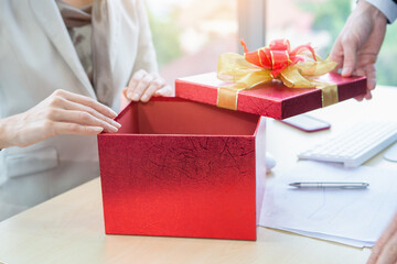 Businessman opening red gift box and giving businesswoman in office