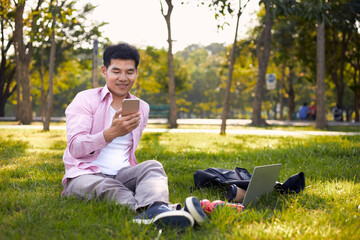 Asian freelance man sitting in a park using his phone on a comfortable working day.