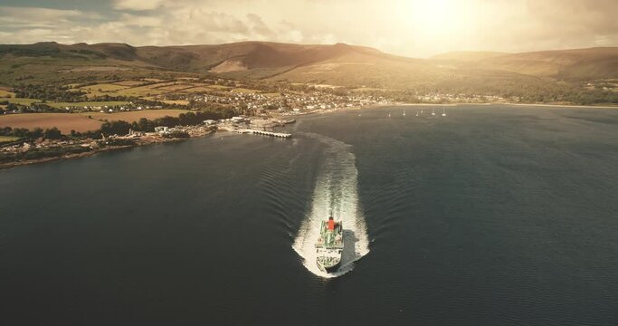 Passenger ferry at ocean bay aerial. Sun nobody nature landscape. Ship cross pier to mainland. Cityscape at green valley. Coast of Firth-of-Clyde Gulf. Brodick Harbor, Arran Island, Scotland, Europe