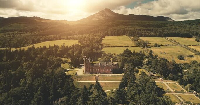 Europe castle at mountains aerial. Nobody nature landscape at historical landmark. Historic architecture attraction of Brodick palace. Designed park, garden at autumn sun day. Arran Island, Scotland