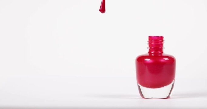 Red nail polish applicator taken from bottle and held until drop falls on surface.