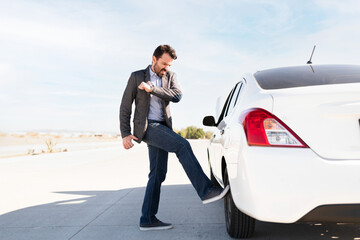 Annoyed latin man kicking the car's flat tire