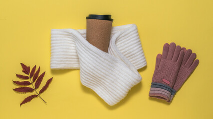 Knitted gloves, a scarf, a glass of coffee and a dried Rowan leaf on a yellow background.