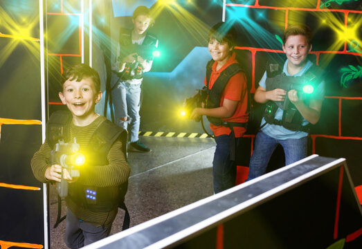 happy active young boy aiming laser gun at other players during lasertag game in dark room