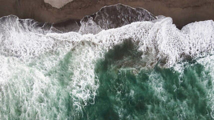 Fototapeta premium Aerial view to waves in beach Splashing Waves with dark sand. Blue turquoise clean wavy sea water.