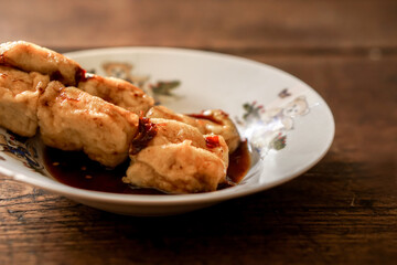 Closeup and crop snack vegan food (fried tofu) in white ceramic plate on wooden background. Thai and Chinese people popular eaten vegan foods in Chinese vegetarian festival in October every years.