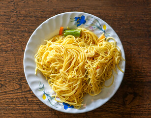 Closeup and top view fried Chinese noodle in white ceramic plate on wooden background. Thai and Chinese people popular eaten vegan foods in Chinese vegetarian festival in October every years