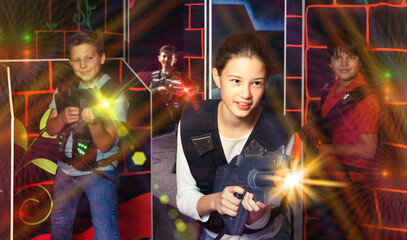 Emotional teen girl with laser pistol playing laser tag with friends on dark room