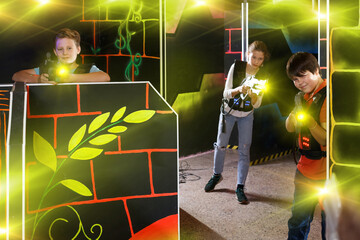 Modern teen girl and boys with laser pistols playing laser tag on dark labyrinth