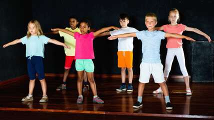 Fototapeta premium Group of cheerful positive little boys and beautiful girls having dancing class in studio in the evening