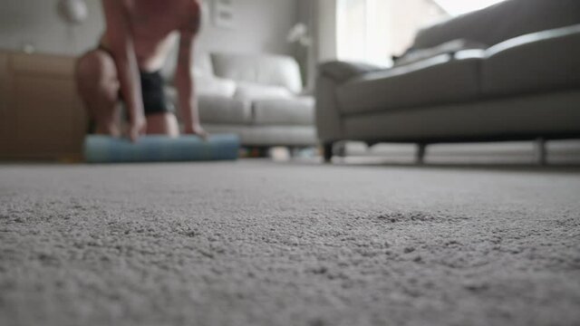 A man rolling out a yoga mat in his living room at home.
