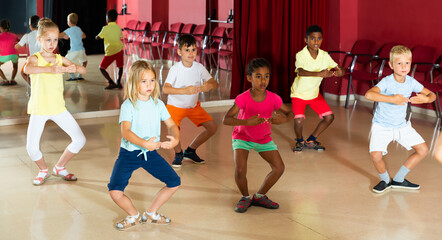 Glad children primary school age rehearsing movements of ballet dance in modern studio