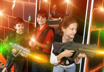 Fototapeta na wymiar Cheerful teenage girl and boys with laser guns playing laser tag on dark room