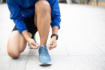 Closeup portrait of a Athlete wearing a blue Windbreaker jacket.,during training tying shoelaces on sporty sneaker . Sport and running idea concept. - obrazy, fototapety, plakaty