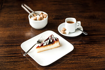 A cheesecake with caramel topping on a white plate, a cup of espresso and a sugar bowl, on a wooden table