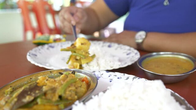 Slow motion of a woman helping herself to indian vegetarian food in the andaman islands at an outdoor restaurant. There is dal, potato, beans and rice.