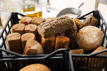Fresh crispy bread in plastic crate and raw ingredients for baking on steel table in bakery