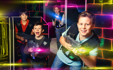 Emotional positive smiling teen boy with laser pistol playing laser tag with friends on dark labyrinth