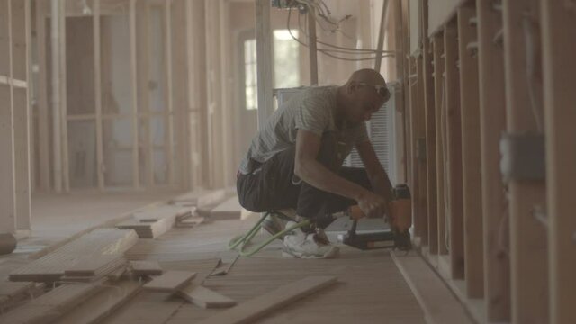 Man is nailing down hardwood flooring at a house