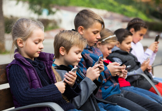 Group of children posing at urban street with mobile devices in autumn