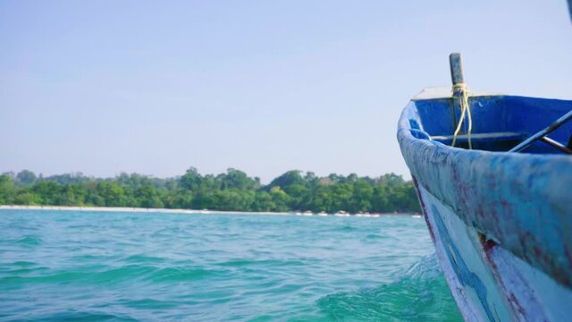 The view toward shore from an old fishing boat with a motor with tourist boats in the distance white sand and remote forest land.