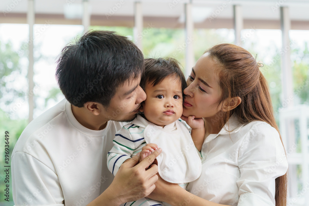 Wall mural asian family happy kiss little baby boy in living room at home, young parent and children enjoy love