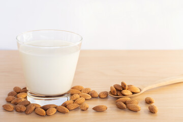 Closeup almond milk in grass and organic raw peeled almond nuts in spoon with laid around cup on wooden background.